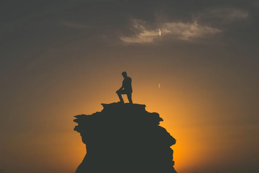 grounded masculine presence Silhouette of a person standing on a mountain peak at sunset