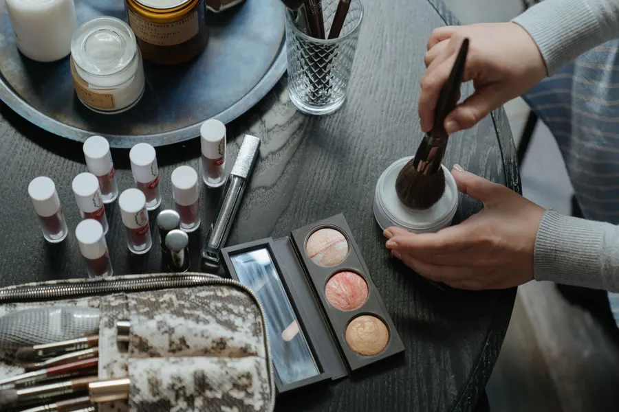 Assorted makeup brushes powders and cosmetic palettes on a clean vanity desk